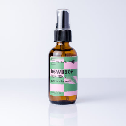 A 2 fl oz amber glass spray bottle of Verdant Wild Tulsi Skin Tonic with a black spray cap and a pastel pink, green, and white label, set against a clean white background with a soft reflection.