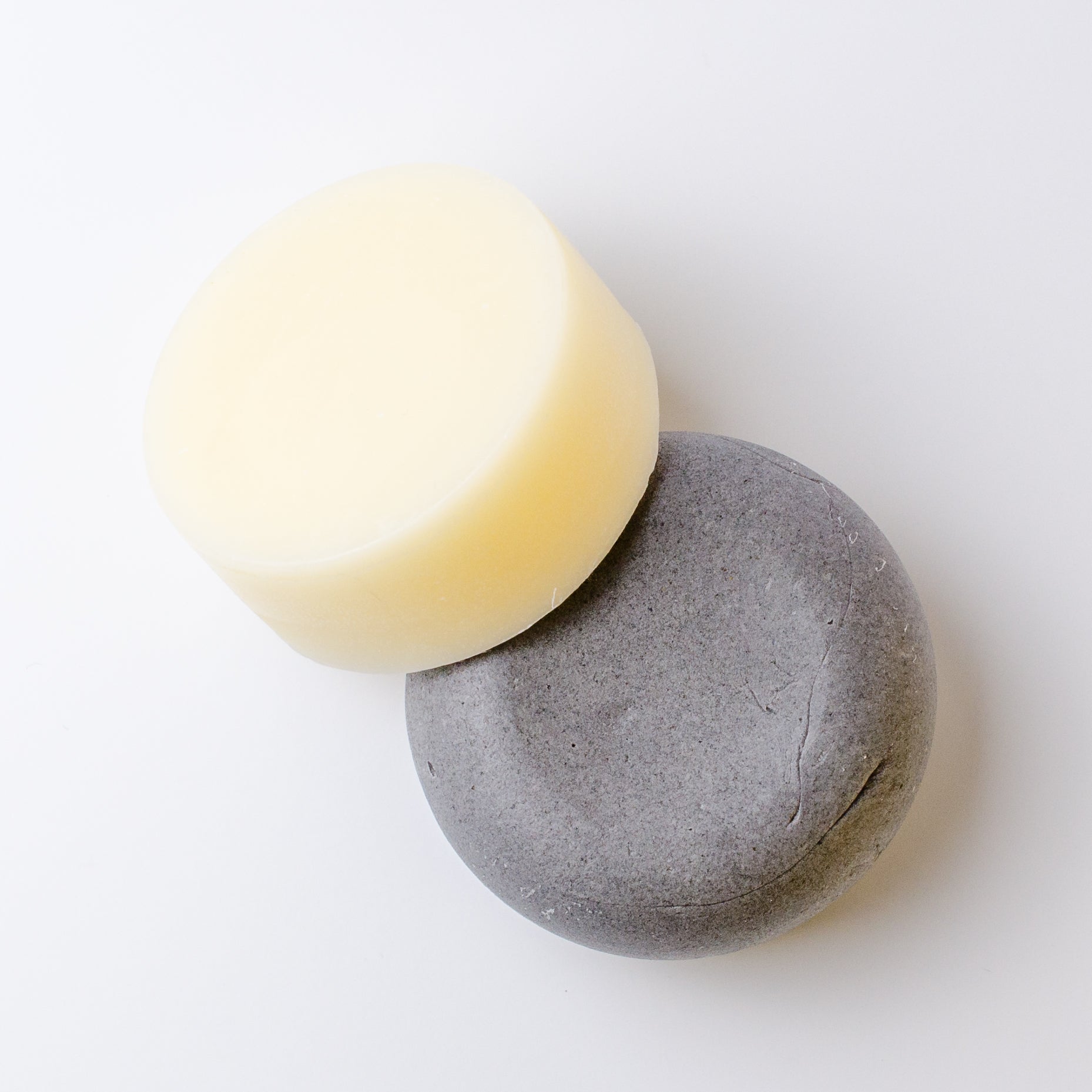 A shampoo and conditioner bar, one pale cream and one dark charcoal gray, arranged overlapping on a clean white background.
