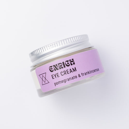 A small clear jar of Enrich Eye Cream with a lavender label and a silver metal lid, photographed on a clean white background.