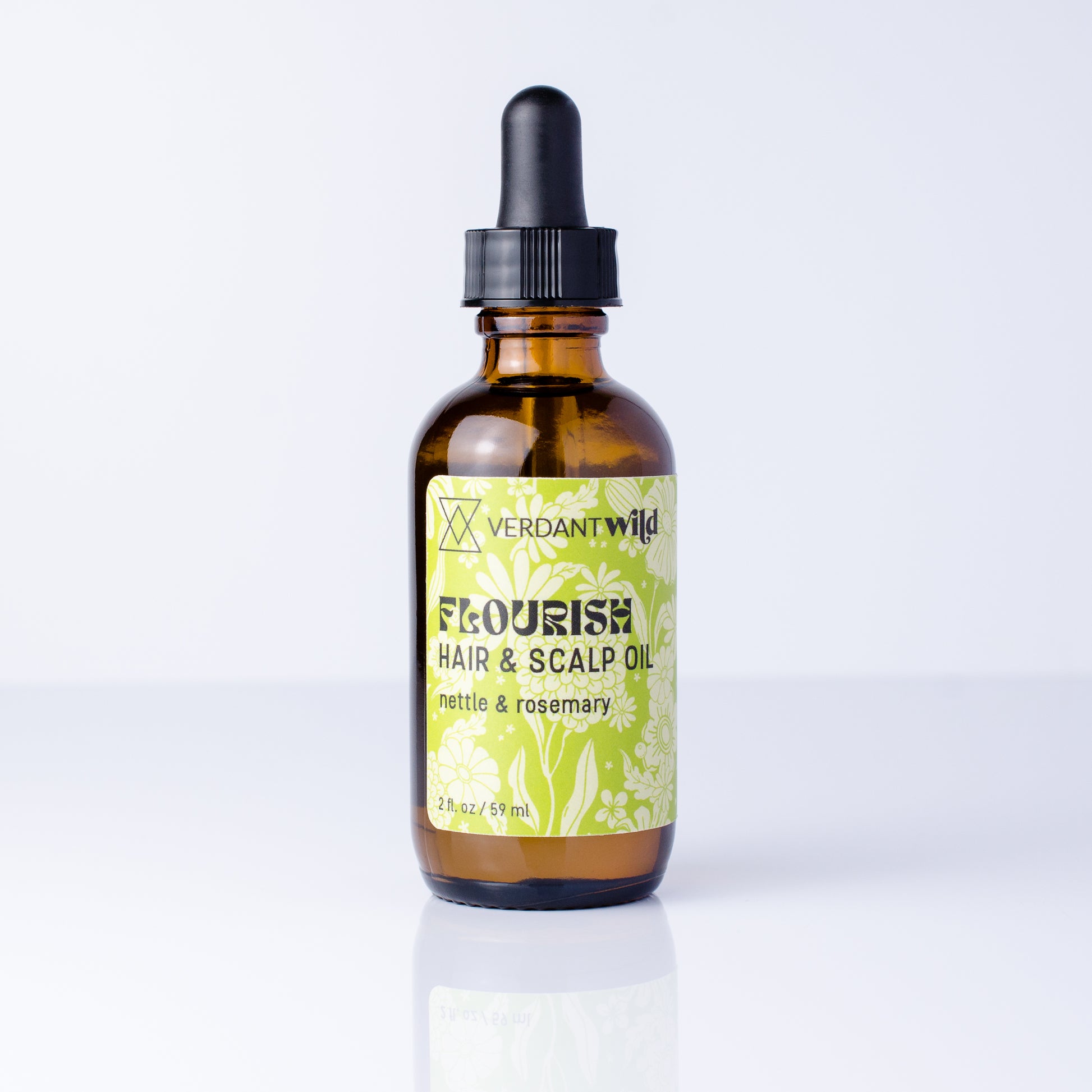 A 2 oz amber glass dropper bottle of Verdant Wild Flourish Hair & Scalp Oil, featuring a light green and white floral label, set against a clean white background with a soft reflection.