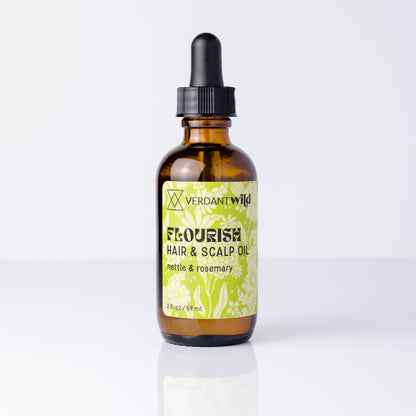 A 2 oz amber glass dropper bottle of Verdant Wild Flourish Hair & Scalp Oil, featuring a black dropper cap and a light green and white floral label, set against a clean white background with a soft reflection.