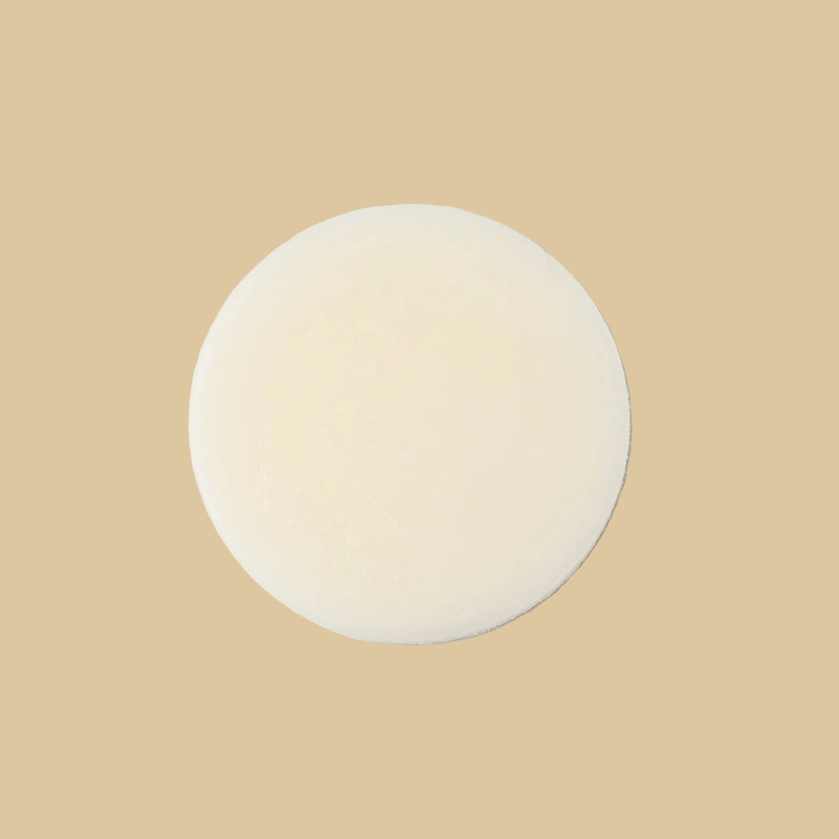 A single round, pale cream-colored conditioner bar, centered on a clean white background.
