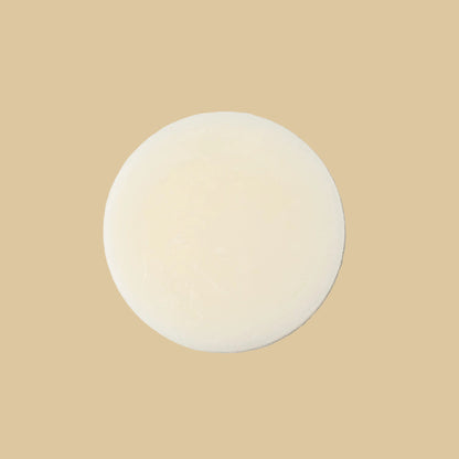 A single round, pale cream-colored conditioner bar, centered on a clean white background.
