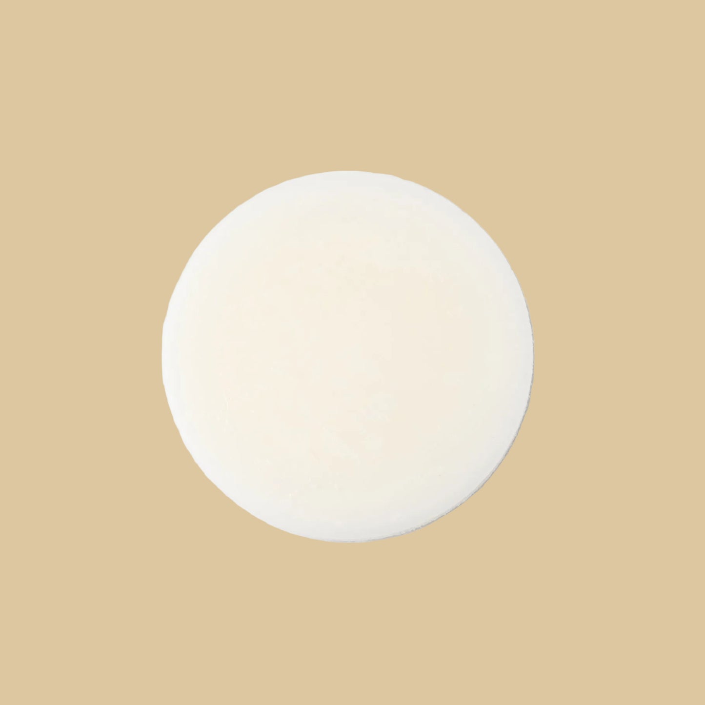 A round, solid bar of conditioner in a cream color, photographed from directly above on a clean background.
