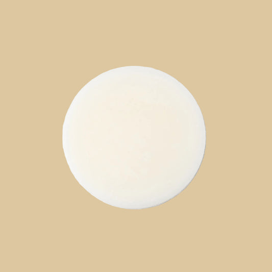 A round, solid bar of conditioner in a cream color, photographed from directly above on a clean background.