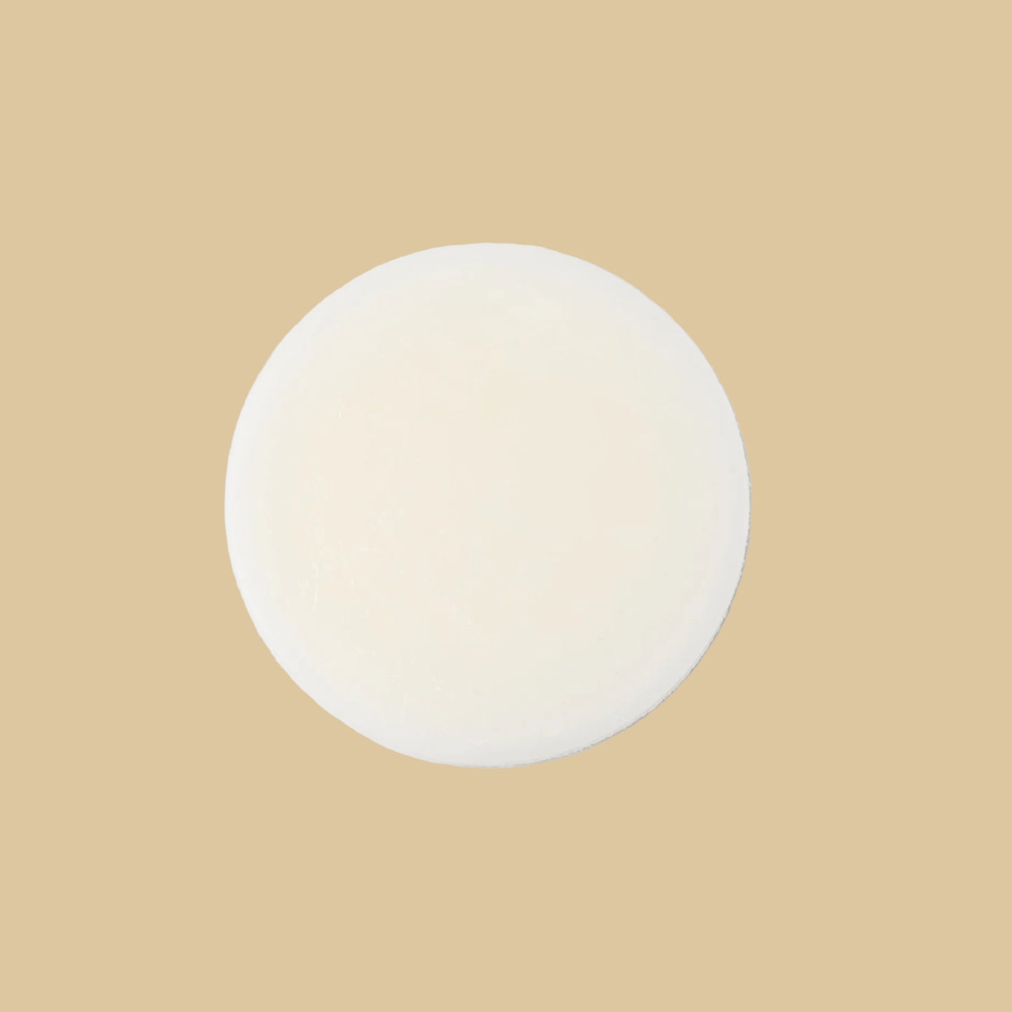 A round, solid bar of conditioner in a cream color, photographed from directly above on a clean background.
