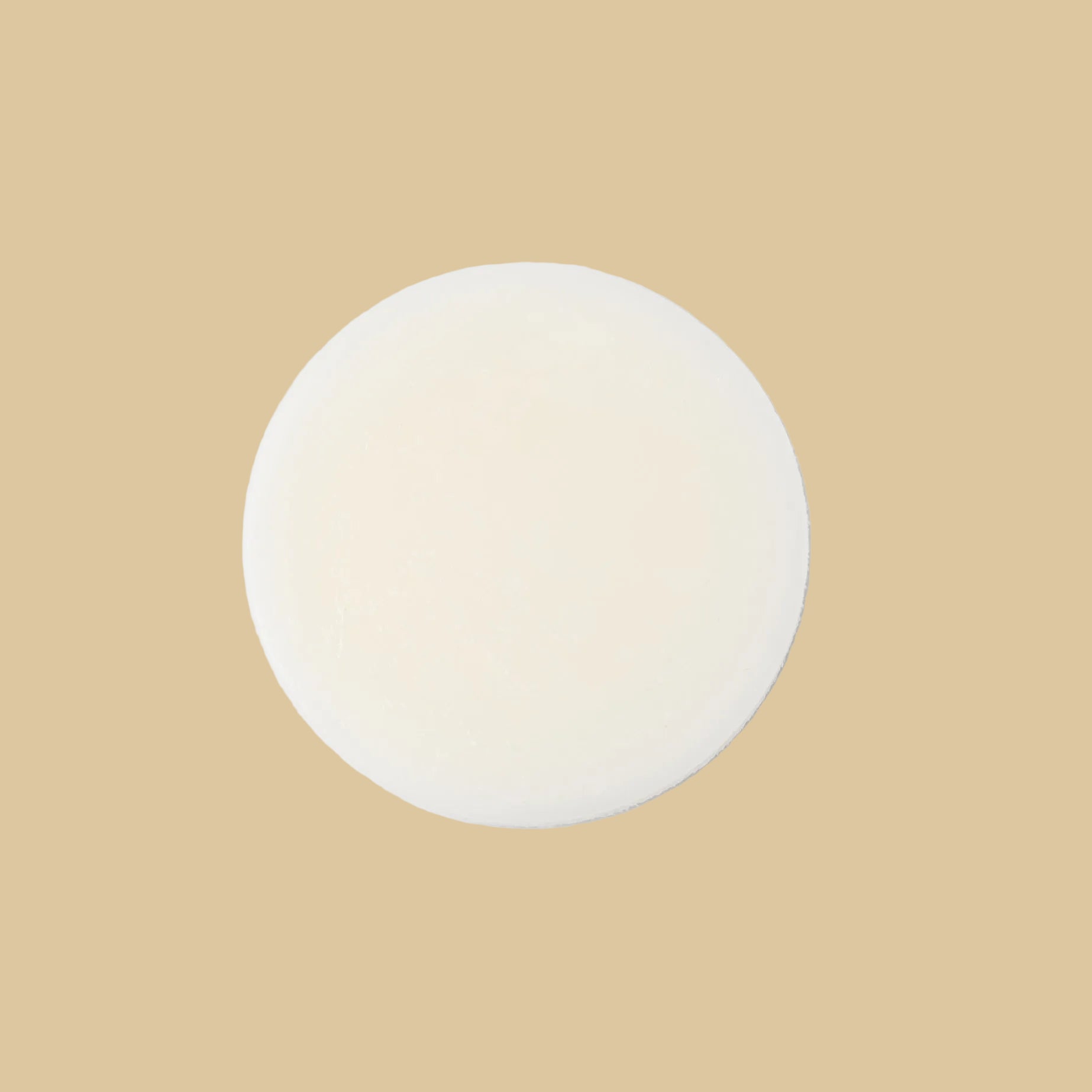 A round, solid bar of conditioner in a cream color, photographed from directly above on a clean background.