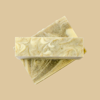 Two stacked rectangular bars of handmade soap with a marbled swirl pattern of cream, olive green, and yellow, set against a plain background.