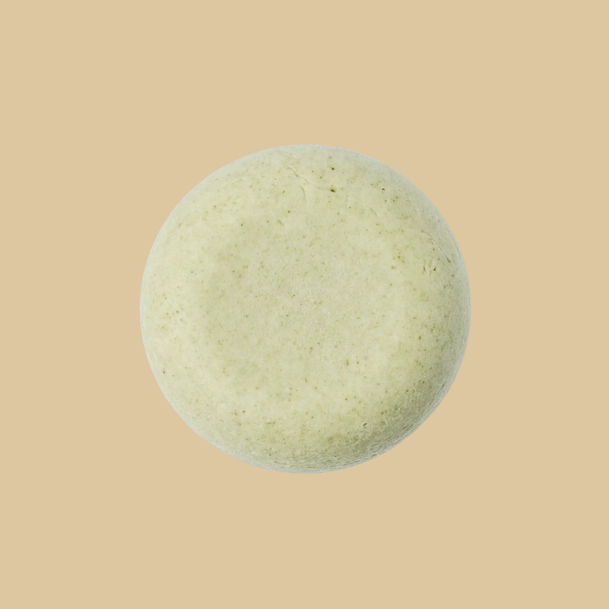 A single round, pale sage green shampoo bar with a textured, matte surface, photographed from directly above on a plain background.