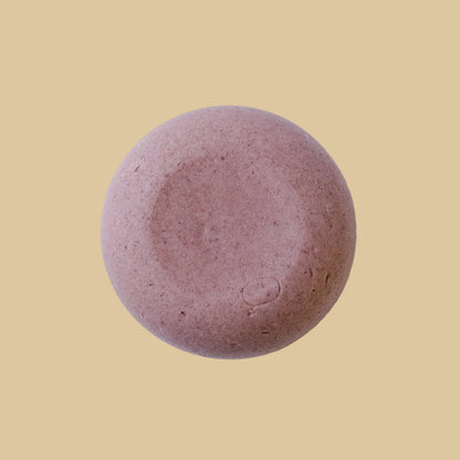 A round, mauve-colored shampoo bar with a matte, textured surface, photographed from directly above on a clean background.