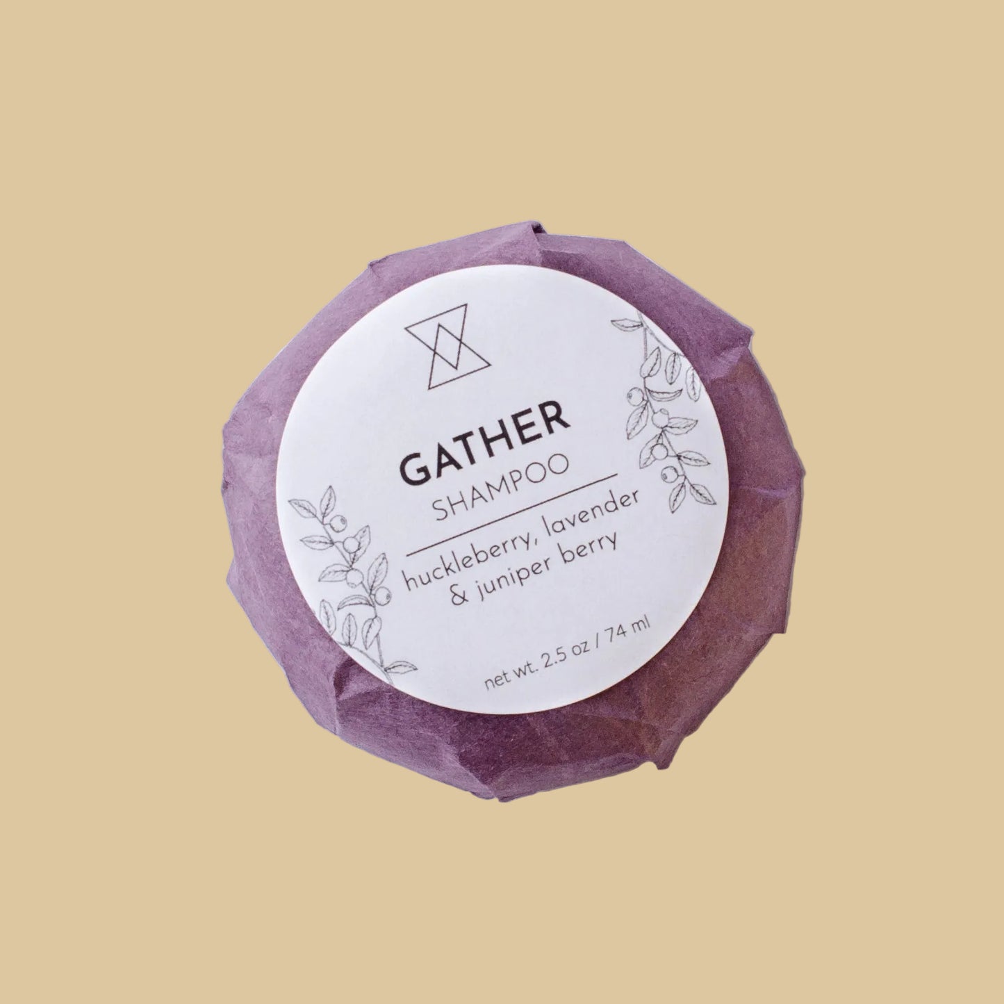 A single wrapped bar of shampoo on a clean background. The product is wrapped in a textured, faceted dusty purple paper wrapper with a white circular label reading 'GATHER SHAMPOO' and 'huckleberry, lavender & juniper berry'.