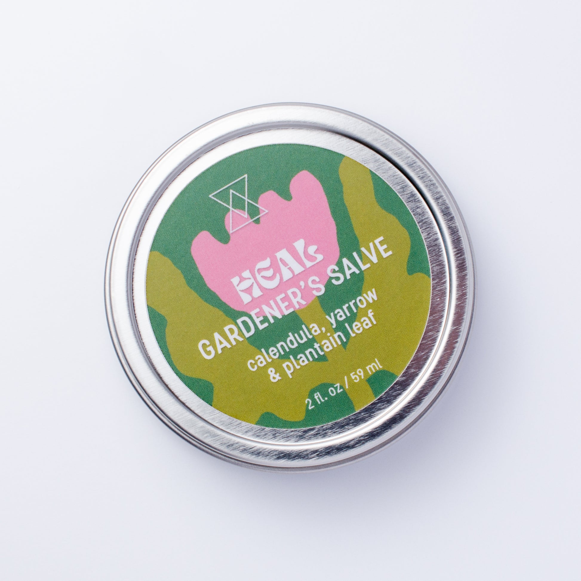 A round silver metal tin of HEAL Gardener's Salve, featuring a colorful label with a pink flower and white text, photographed on a clean white background.