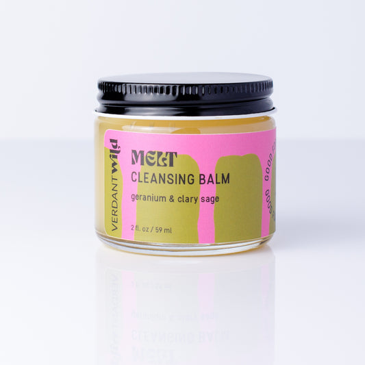 A jar of Verdant Wild MELT Cleansing Balm with a black lid, featuring a pink and olive green label, set against a clean white background with a soft reflection.