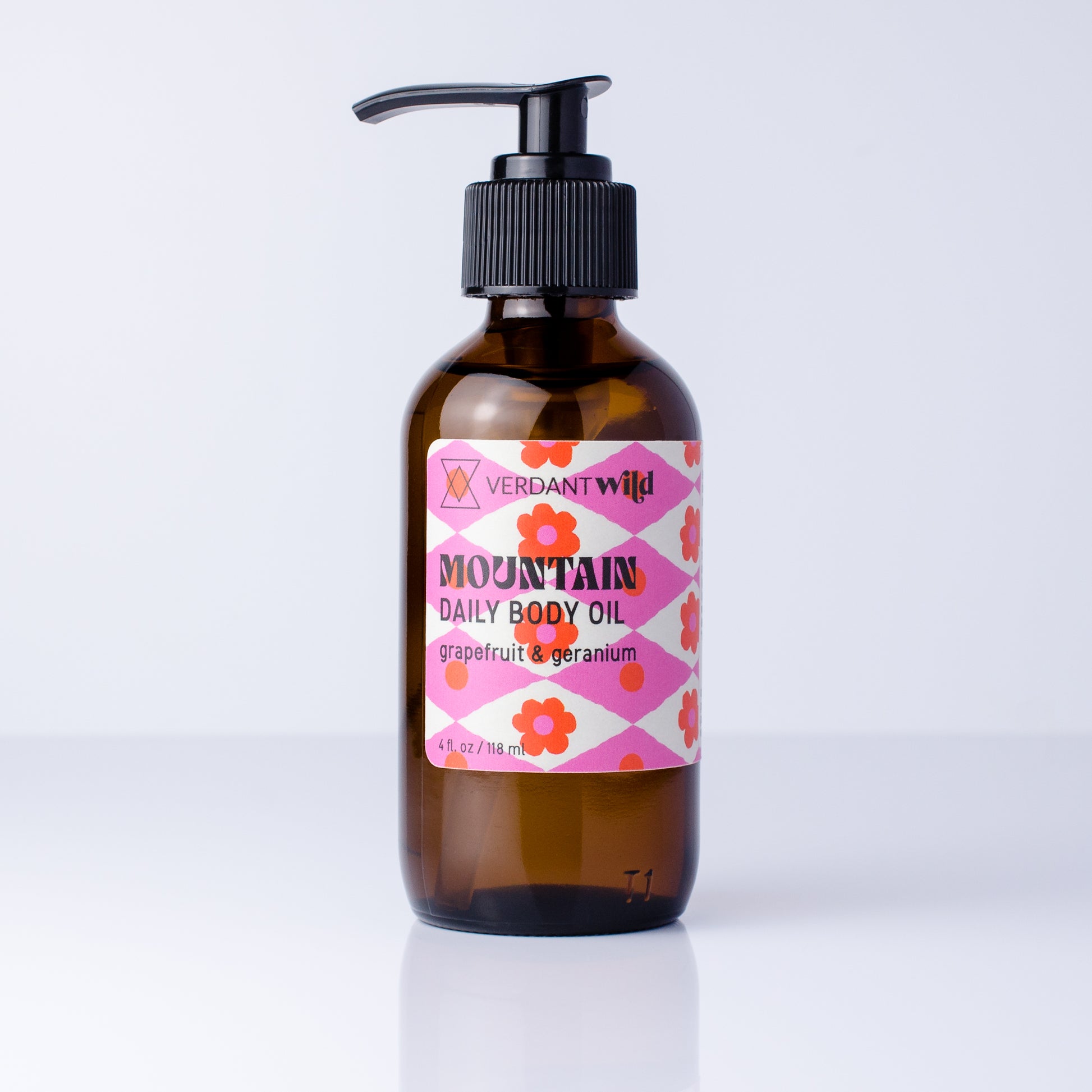 A 4 oz amber glass pump bottle of Verdant Wild Mountain Daily Body Oil with a pink and white patterned label, set against a clean white background.