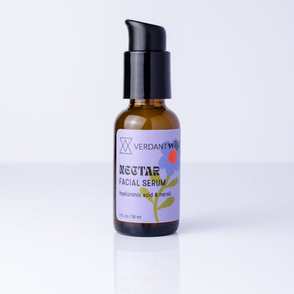 A small amber glass bottle of Verdant Wild Nectar Facial Serum with a black pump dispenser, set against a clean white background with a soft reflection.
