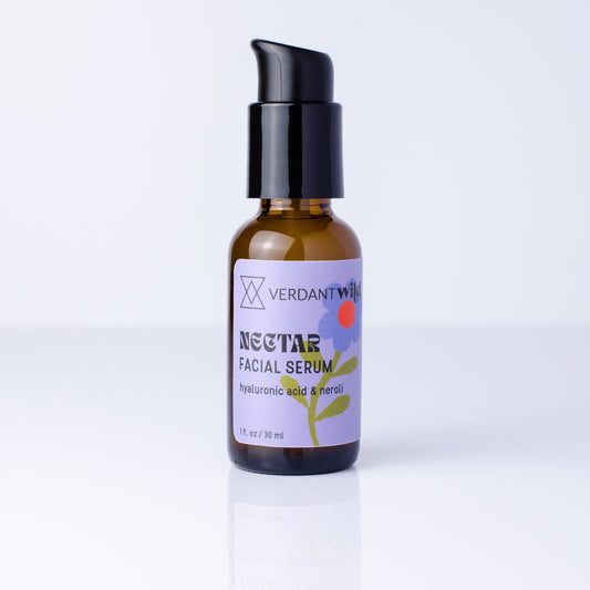 A small amber glass bottle of Verdant Wild Nectar Facial Serum with a black pump dispenser, set against a clean white background with a soft reflection.