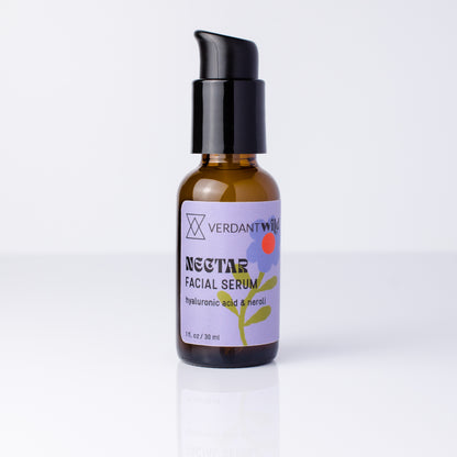 A 30 ml amber glass bottle of Verdant Wild Nectar Facial Serum with a black pump dispenser and a lavender label, set against a clean white background with a soft reflection.