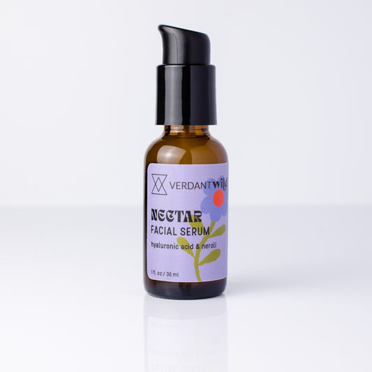 A 30 ml amber glass bottle of Verdant Wild Nectar Facial Serum with a black pump dispenser and a lavender label, set against a clean white background with a soft reflection.