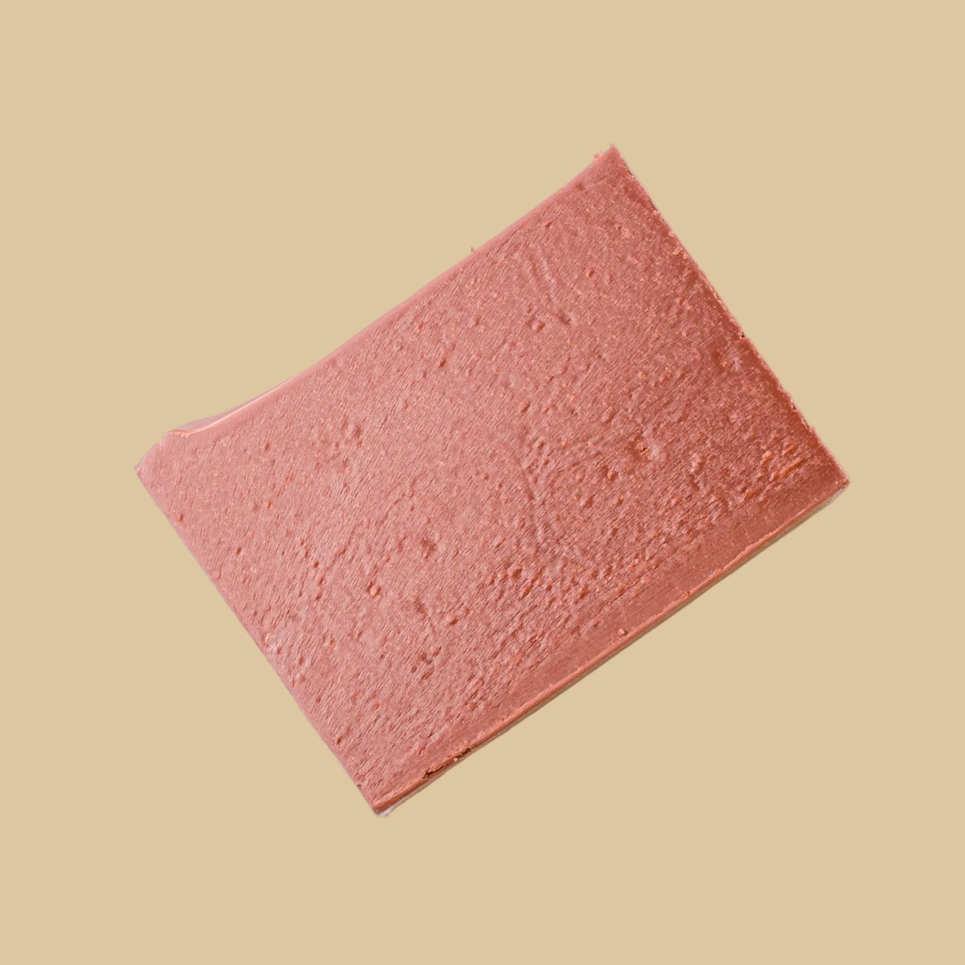 A rectangular pink textured sponge or foam pad shown at an angle on a solid beige background.
