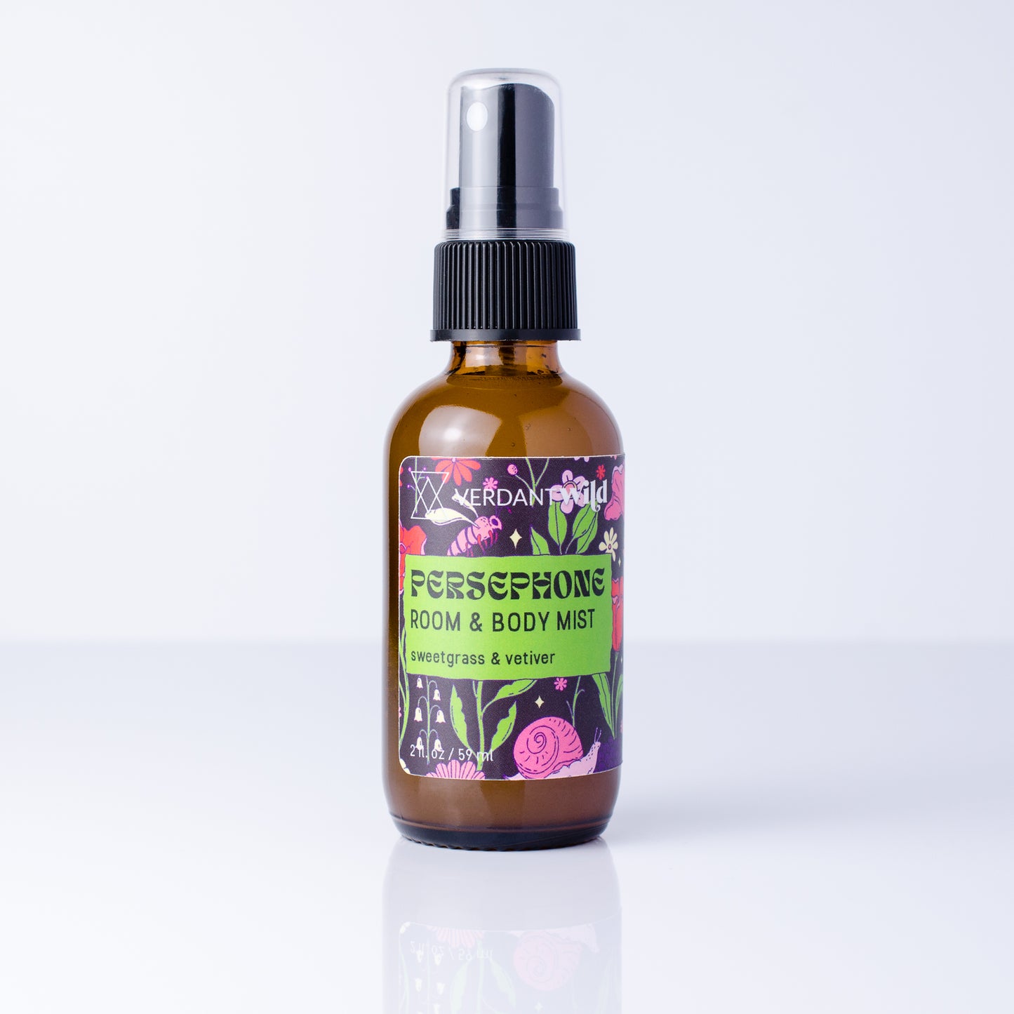 An amber glass room and body mist spray bottle with a black spray cap and a colorful label reading 'Persephone Room & Body Mist' by Verdant Wild, shown on a clean white background with a soft reflection.