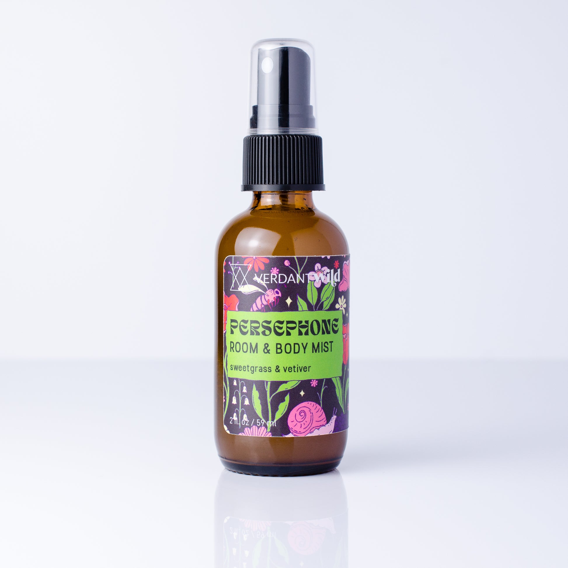 An amber glass room and body mist spray bottle with a black spray cap and a colorful label reading 'Persephone Room & Body Mist' by Verdant Wild, shown on a clean white background with a soft reflection.