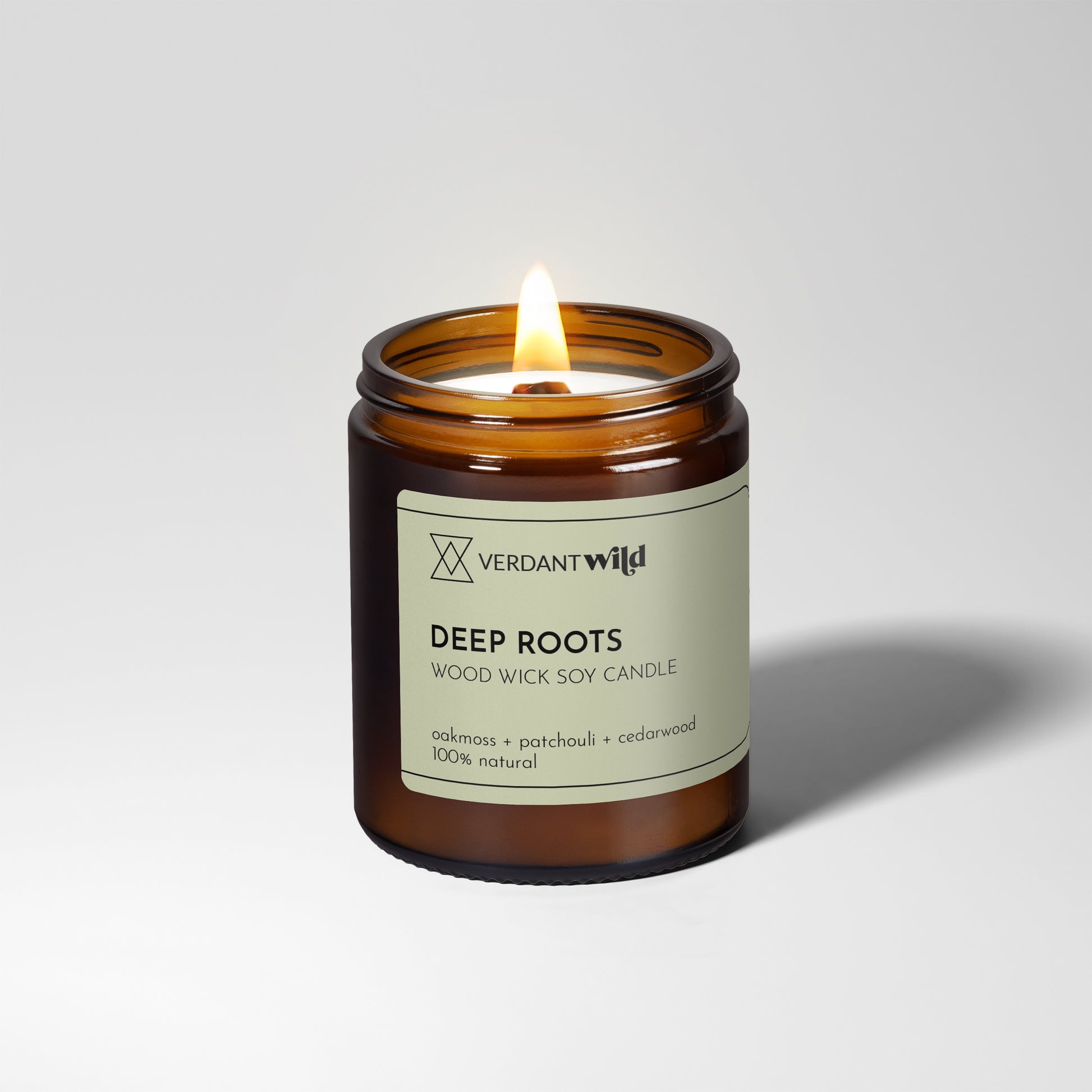 Verdant Wild Deep Roots candle with a lit wick on a white background