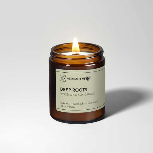 Verdant Wild Deep Roots candle with a lit wick on a white background
