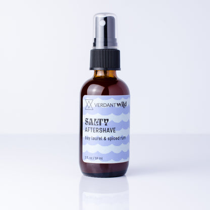 A 2 fl oz amber glass spray bottle of Verdant Wild Salty Aftershave with a black pump, set on a white background.