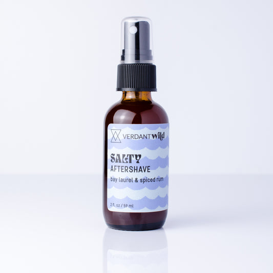 A 2 fl oz amber glass spray bottle of Verdant Wild Salty Aftershave with a black pump, set on a white background.