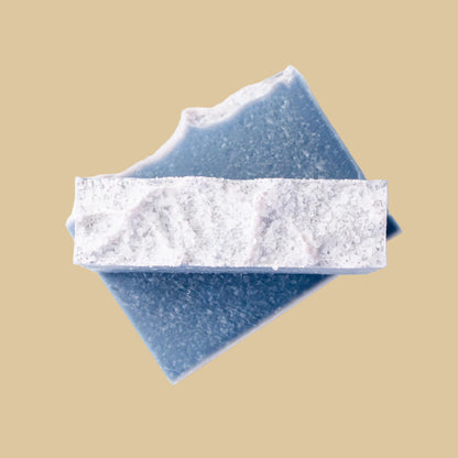 Two rectangular blue soap bars stacked diagonally, with one bar showing the top dusted with sparkly sea salt.