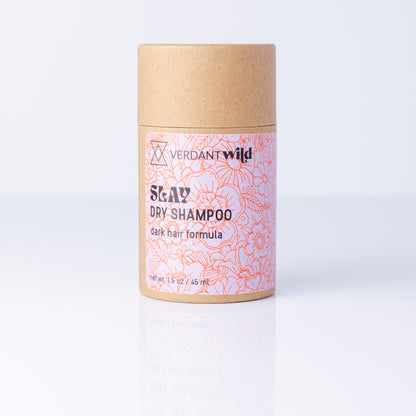 A cylindrical cardboard container of Verdant Wild Slay Dry Shampoo, featuring a kraft brown top and bottom with a pink and red floral patterned label, set against a clean white background with a soft reflection.