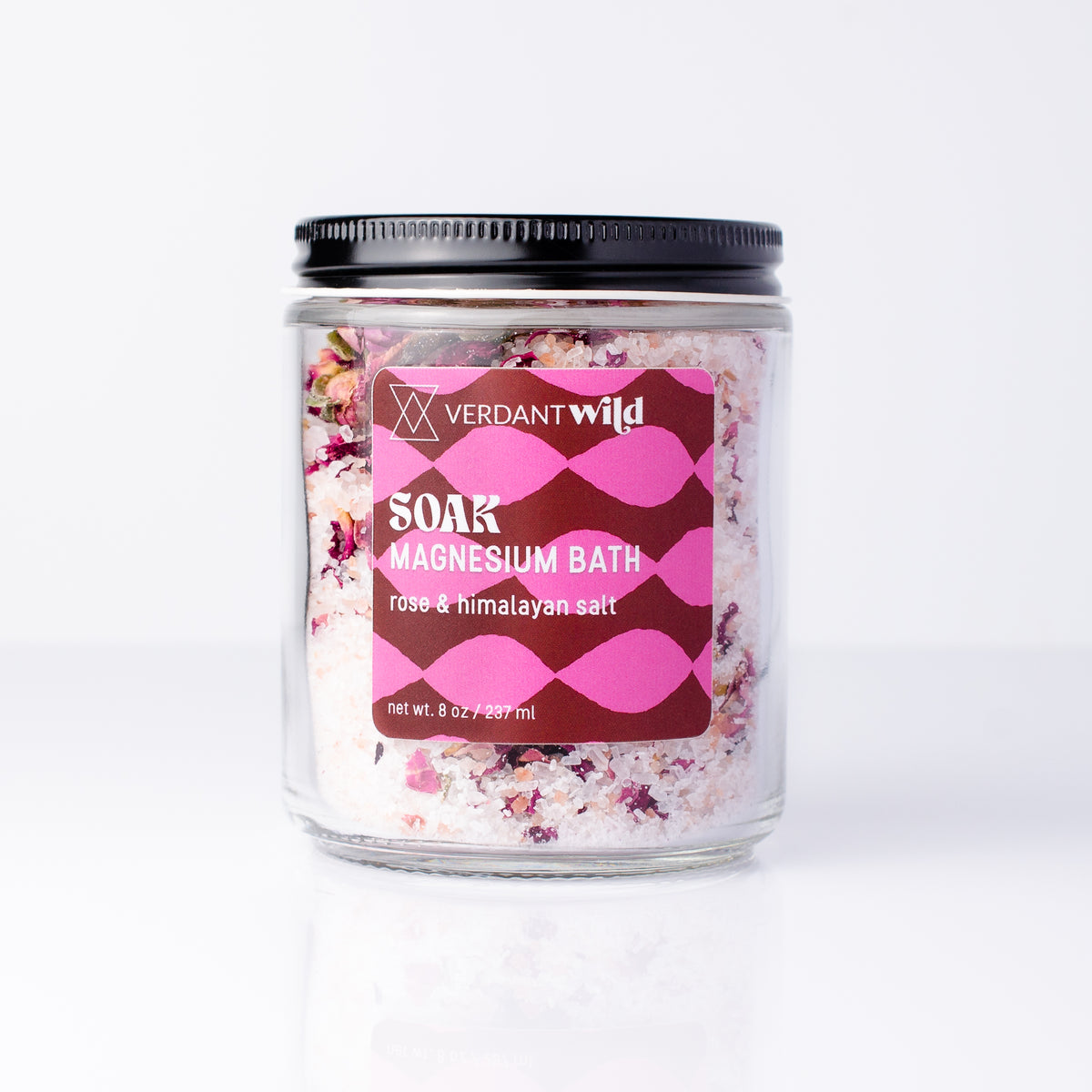 A clear glass jar of Verdant Wild Soak Magnesium Bath in rose & himalayan salt, featuring a black screw-on lid and a pink and burgundy label, set against a clean white background.
