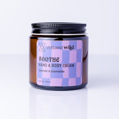 A jar of Verdant Wild Soothe Hand & Body Cream, lavender & chamomile, in an amber glass jar with a black lid and a blue and purple checkered label, set against a clean white background with a soft reflection.