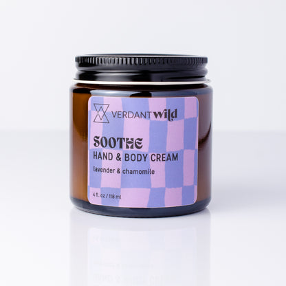 An amber glass jar of Verdant Wild Soothe Hand & Body Cream with a black lid and a lavender and purple checkered label, set against a clean white background with a soft reflection.