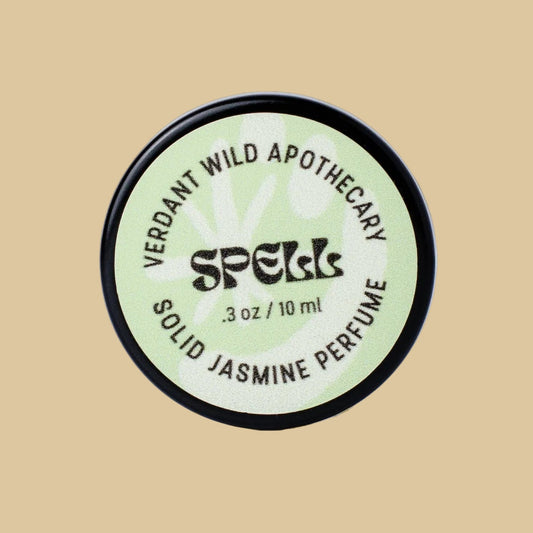 A round black-lidded jar of Verdant Wild Apothecary Spell Solid Jasmine Perfume, featuring a pale green label with black text.
