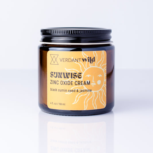 A jar of Verdant Wild Sunrise Zinc Oxide Cream with a black lid and a yellow label featuring a sun illustration, set against a clean white background with a soft reflection.
