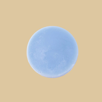 A round, light blue conditioner bar, photographed from directly above on a clean background.