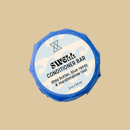 A round wrapped bar of Swell Conditioner soap on a clean background. The bar is wrapped in blue paper and features a white circular label with black text reading 'Swell Conditioner' and botanical line drawings.