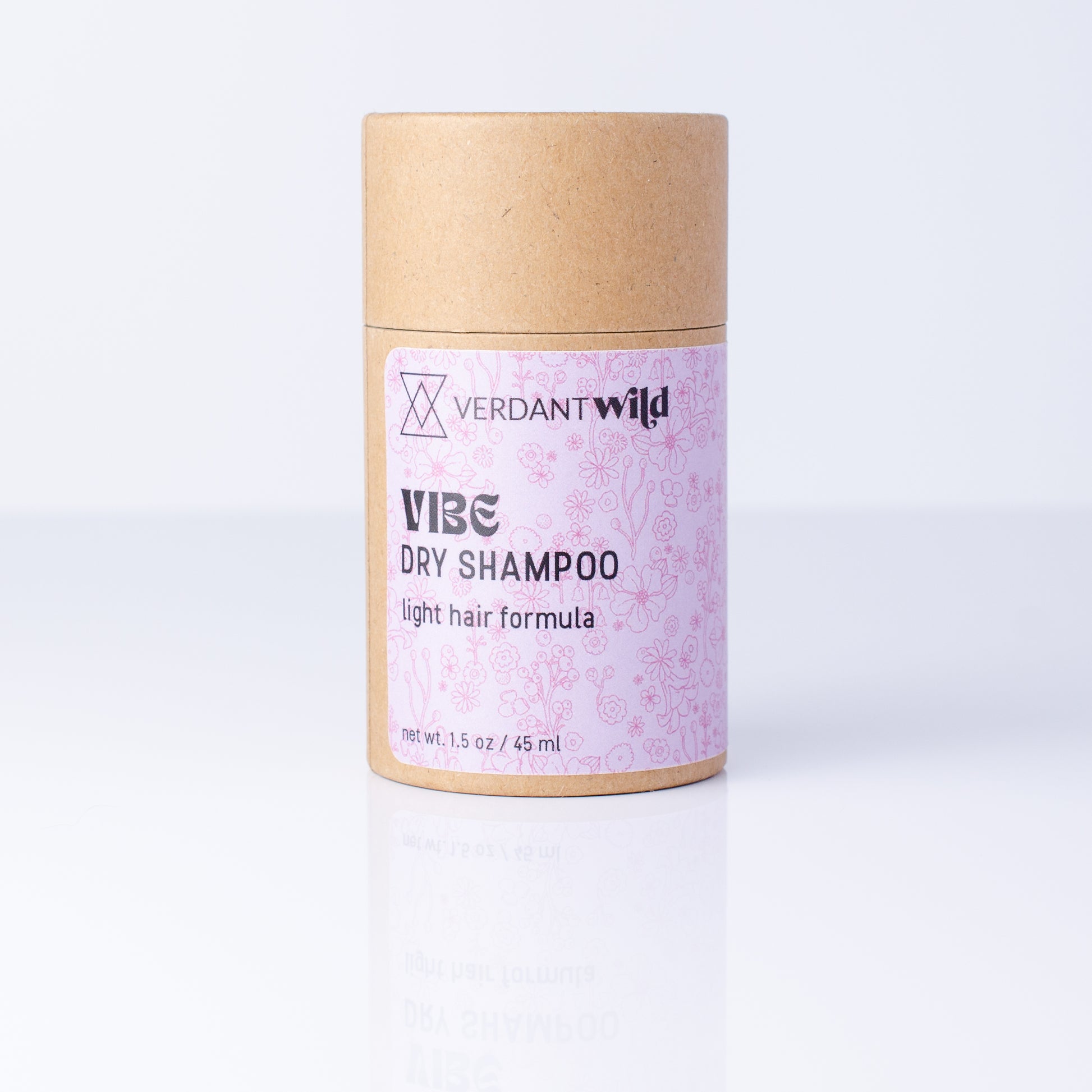 A cylindrical cardboard tube of Verdant Wild Vibe Dry Shampoo, featuring a light pink patterned label, set against a clean white background with a soft reflection.
