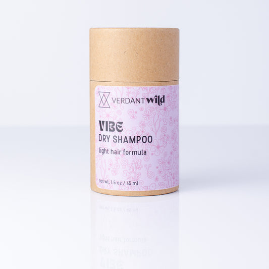 A cylindrical cardboard tube of Verdant Wild Vibe Dry Shampoo, featuring a light pink patterned label, set against a clean white background with a soft reflection.